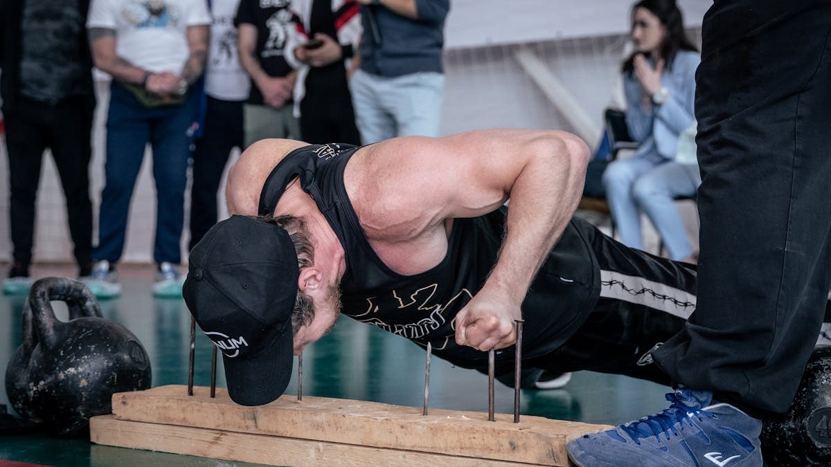 Muscular man performing knuckle push-up at karate festival event indoors, showcasing strength and determination.